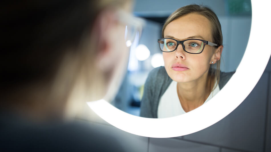 A beautiful woman with glasses looking at herself in the mirror.