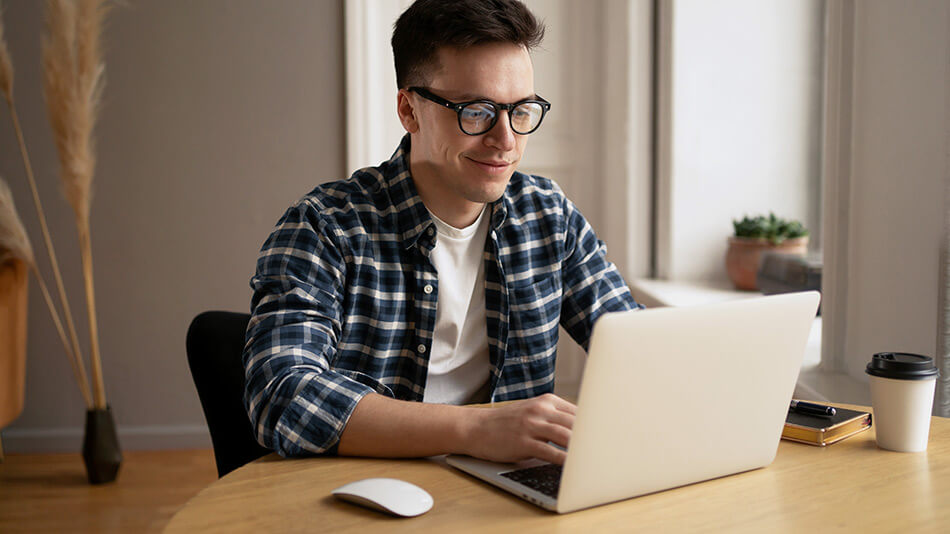 A young man with glasses looking at his laptop in the living room.